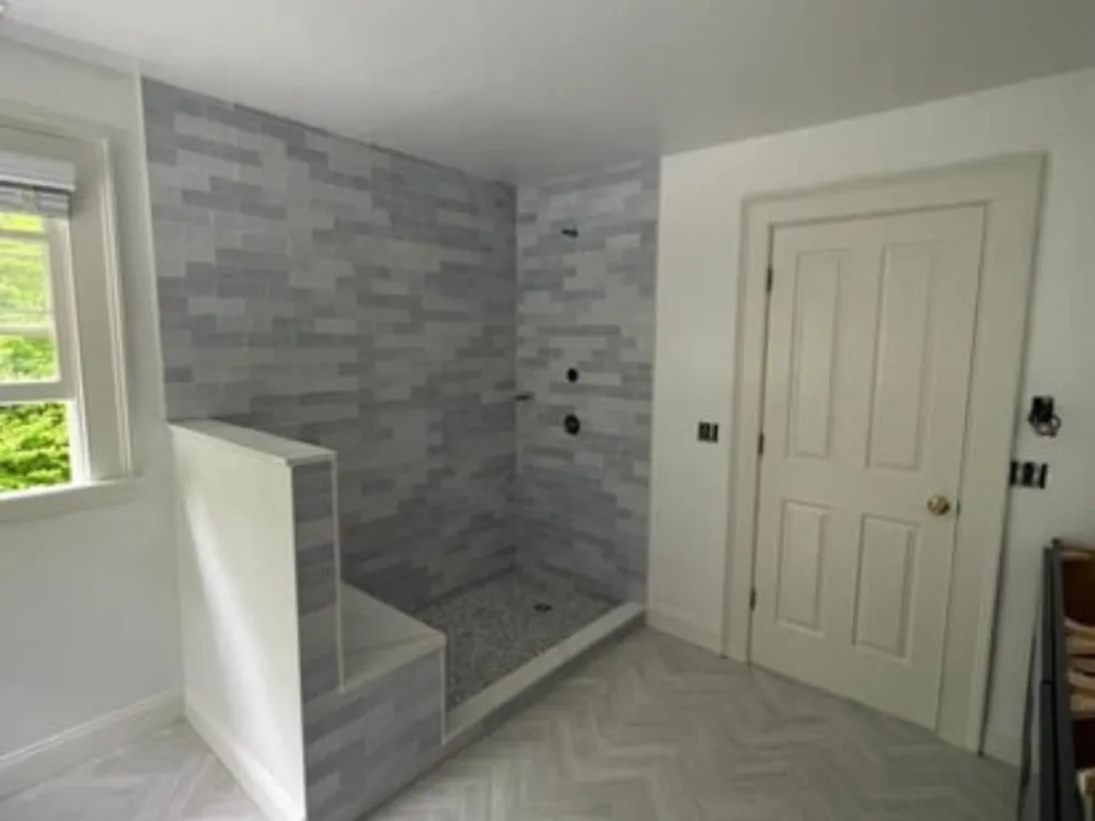 Bathroom painting in progress with tiled shower area and white walls, showcasing a modern, clean design.