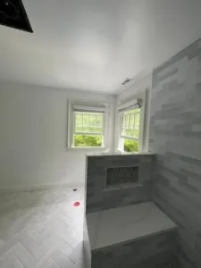 Newly painted bathroom with soft gray tile and natural light from two large windows.