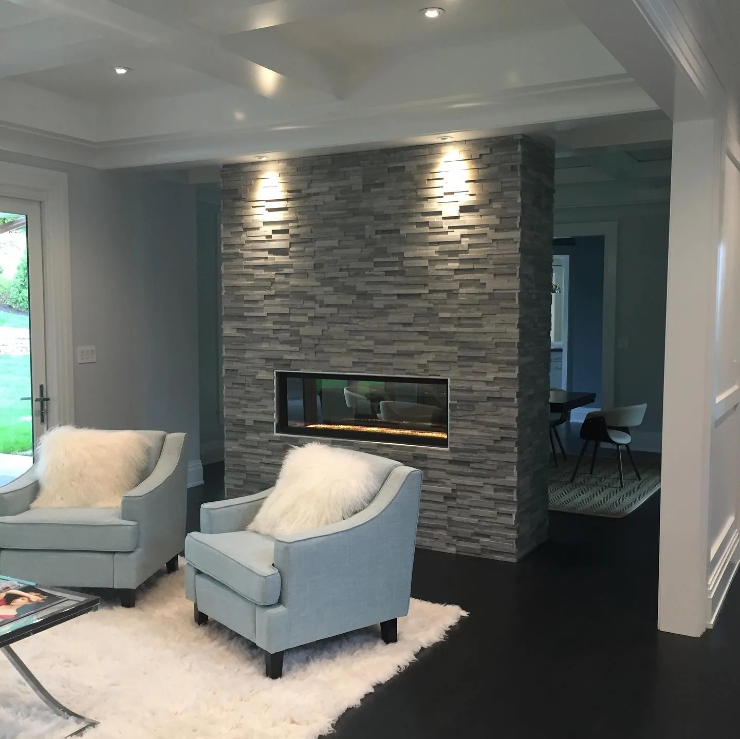 Close-up of a modern stacked stone fireplace with finished custom coffered ceilings and blue chairs.